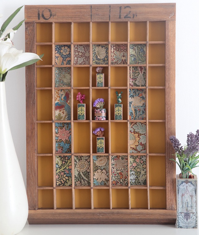 Decorative colourful display of william morris prints and little wooden vases in an old letterpress printers type case drawer tray