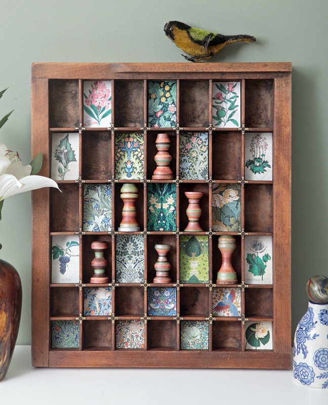 Little quirky display of hand turned wooden vases and decorative prints in vintage antique printers tray type case